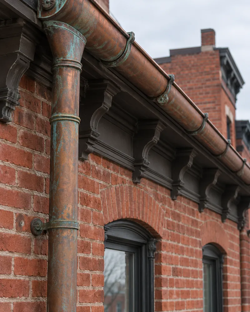 Copper half-round gutter and round leader on a brick wall